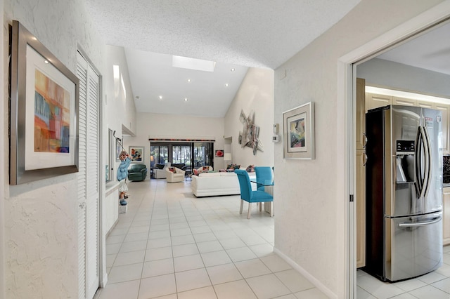 corridor featuring light tile patterned floors, a textured ceiling, and a skylight