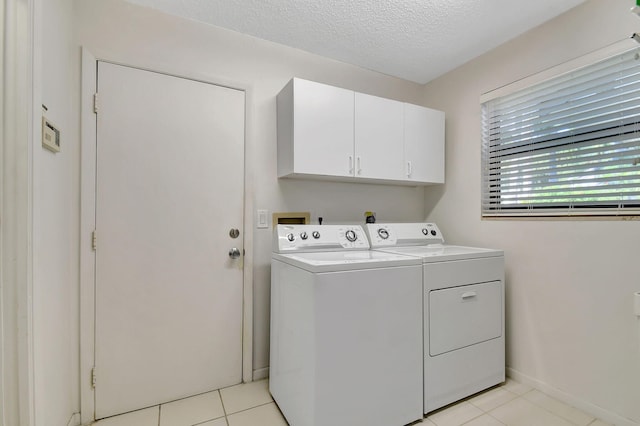 laundry room featuring cabinets, light tile patterned floors, a textured ceiling, and washing machine and clothes dryer