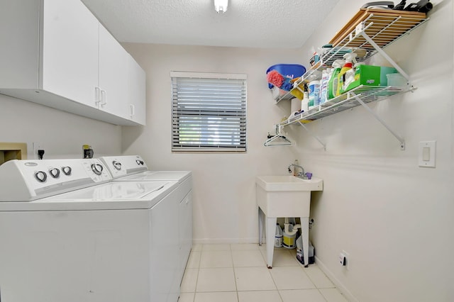 washroom with washing machine and dryer, light tile patterned floors, cabinets, and a textured ceiling