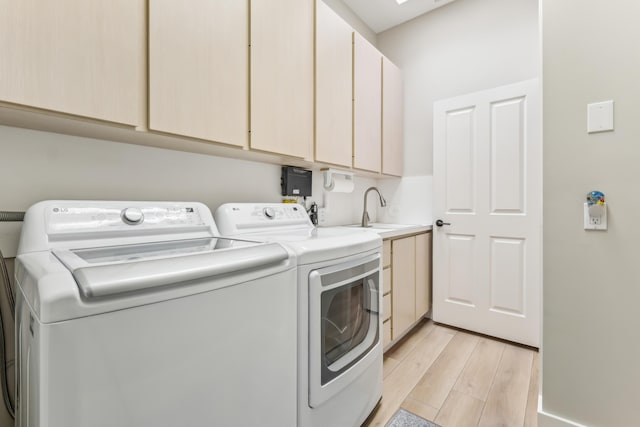 laundry area featuring cabinets, independent washer and dryer, sink, and light hardwood / wood-style flooring