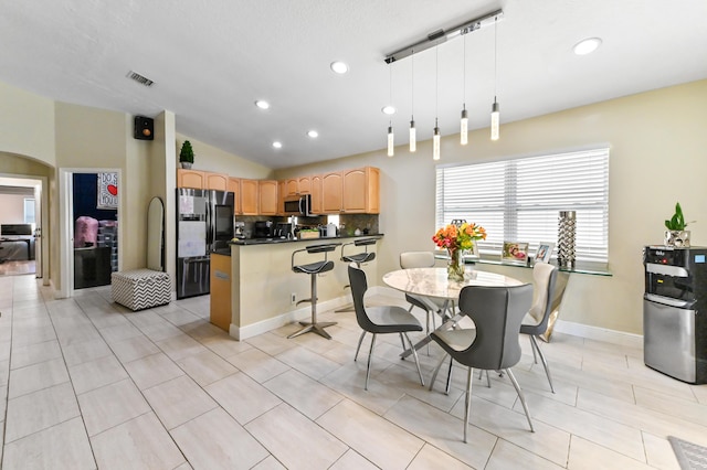 kitchen featuring light brown cabinetry, tasteful backsplash, stainless steel appliances, vaulted ceiling, and pendant lighting