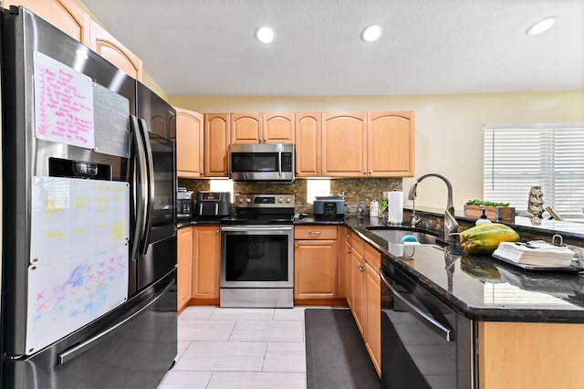 kitchen with sink, backsplash, dark stone countertops, light tile patterned floors, and appliances with stainless steel finishes