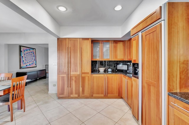 kitchen with paneled built in fridge, dark stone countertops, light tile patterned floors, and tasteful backsplash