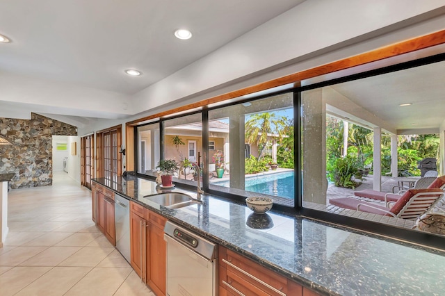 kitchen featuring stainless steel dishwasher, light tile patterned floors, sink, and dark stone counters