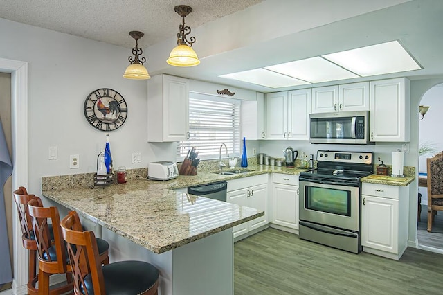 kitchen with kitchen peninsula, appliances with stainless steel finishes, sink, pendant lighting, and white cabinetry