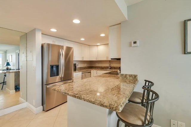 kitchen with a kitchen breakfast bar, kitchen peninsula, light tile patterned floors, appliances with stainless steel finishes, and white cabinetry