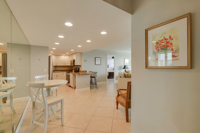 kitchen featuring a breakfast bar, white cabinets, light tile patterned flooring, kitchen peninsula, and stainless steel appliances