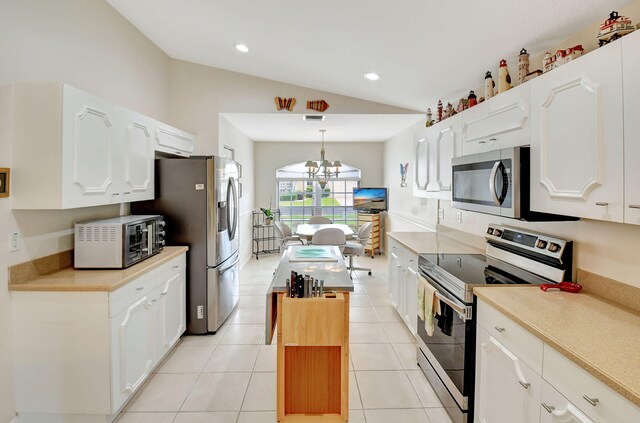 kitchen with stainless steel appliances, vaulted ceiling, white cabinets, a chandelier, and hanging light fixtures