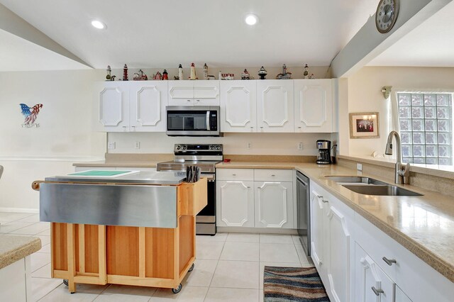 kitchen featuring stainless steel appliances, vaulted ceiling, sink, light tile patterned floors, and white cabinets