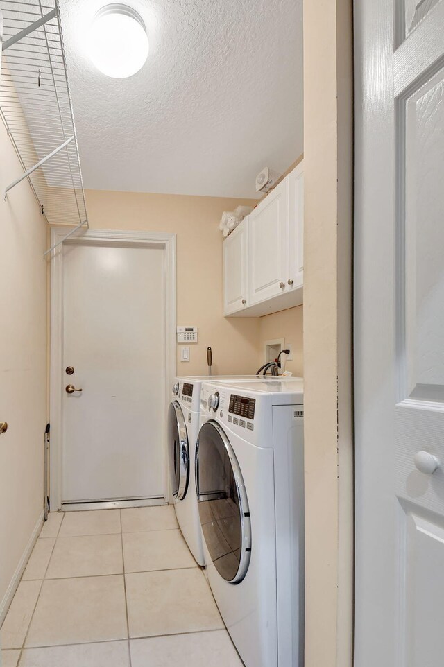 laundry area featuring washing machine and clothes dryer, light tile patterned flooring, cabinets, and a textured ceiling