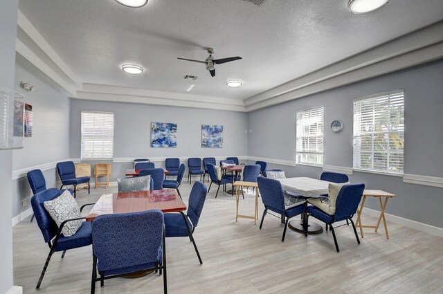 dining area featuring ceiling fan, a raised ceiling, light wood-type flooring, and a textured ceiling