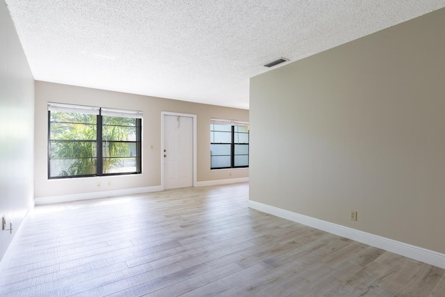 spare room with a healthy amount of sunlight, a textured ceiling, and light hardwood / wood-style floors