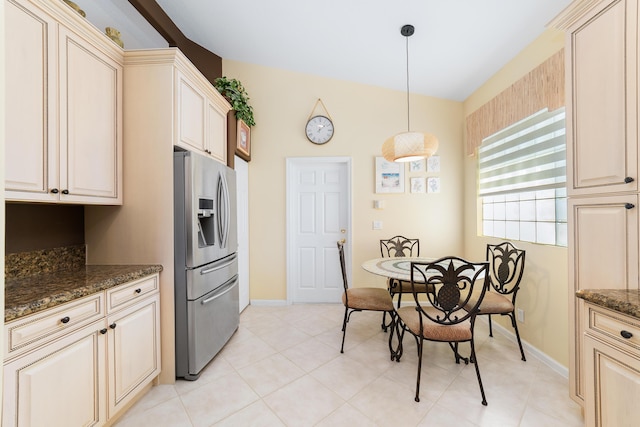 kitchen featuring cream cabinetry, dark stone counters, stainless steel fridge, decorative light fixtures, and light tile patterned flooring