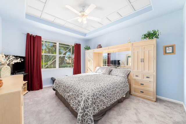 bedroom with ceiling fan, a tray ceiling, and light carpet