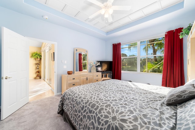 carpeted bedroom featuring ceiling fan and a tray ceiling