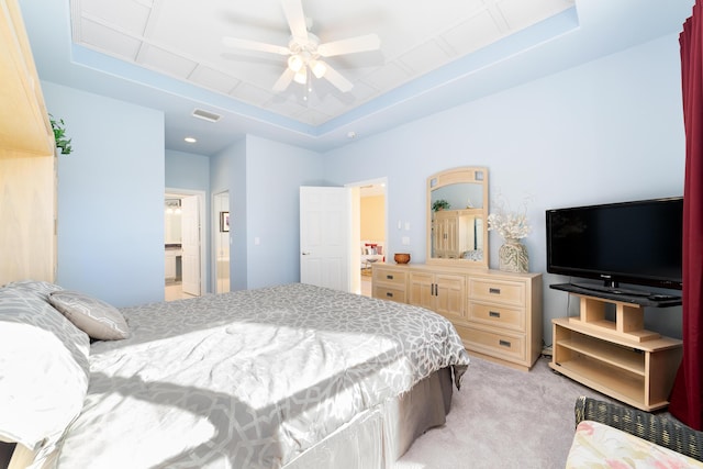 carpeted bedroom featuring ensuite bathroom, a raised ceiling, and ceiling fan