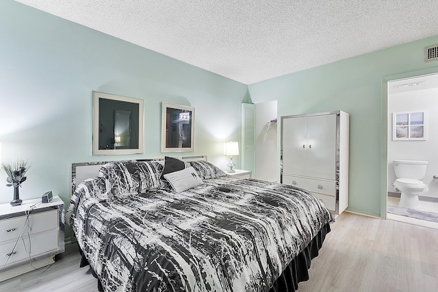 bedroom featuring ensuite bath, a textured ceiling, and light wood-type flooring