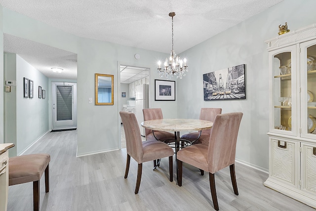 dining room featuring light wood-type flooring, a textured ceiling, and an inviting chandelier