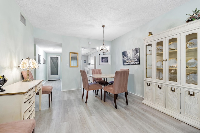 dining area with light hardwood / wood-style floors, a textured ceiling, and an inviting chandelier