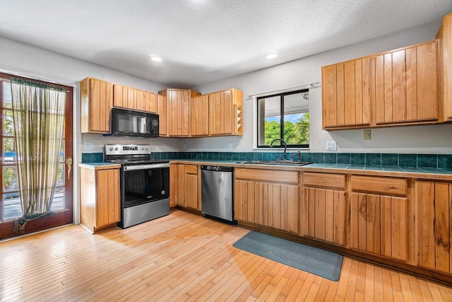 kitchen with sink, light wood-type flooring, a textured ceiling, appliances with stainless steel finishes, and tile counters