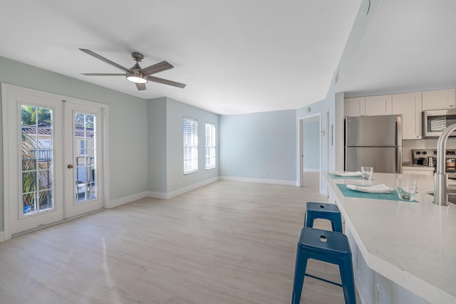 kitchen with appliances with stainless steel finishes, light wood-type flooring, ceiling fan, french doors, and a kitchen bar