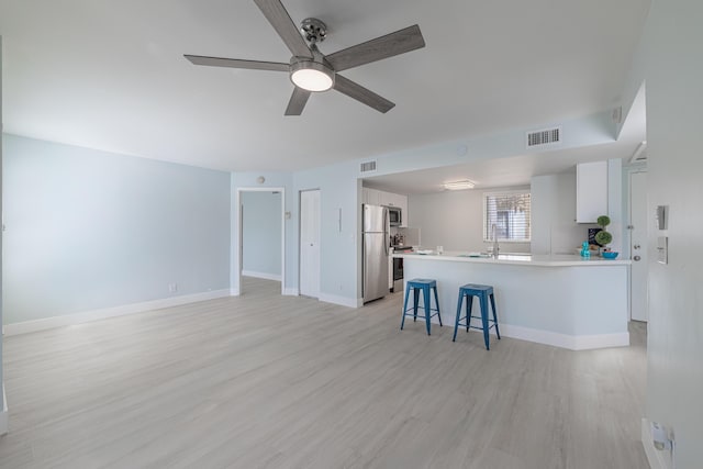 kitchen with kitchen peninsula, a breakfast bar, white cabinets, appliances with stainless steel finishes, and ceiling fan