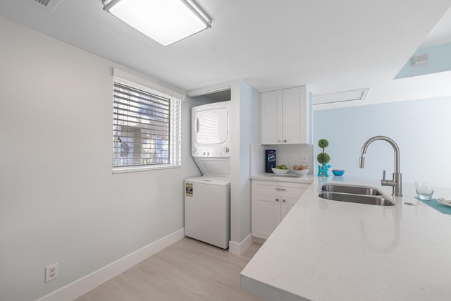 kitchen featuring sink, white cabinetry, light hardwood / wood-style floors, and stacked washer / dryer