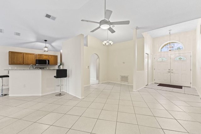 foyer with ceiling fan with notable chandelier, light tile patterned flooring, and lofted ceiling