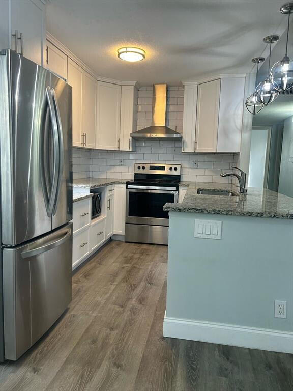 kitchen with sink, wall chimney exhaust hood, dark stone countertops, white cabinets, and appliances with stainless steel finishes