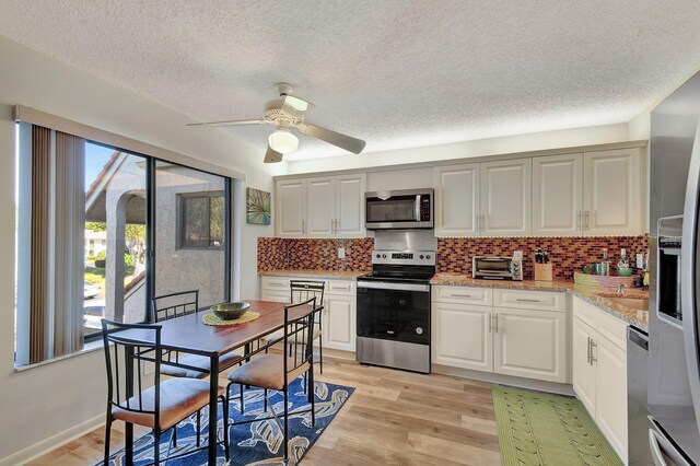 kitchen with white cabinets, light hardwood / wood-style flooring, light stone countertops, appliances with stainless steel finishes, and tasteful backsplash