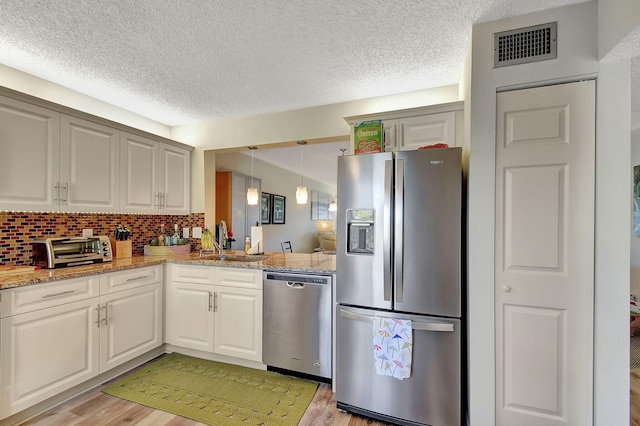 kitchen with white cabinets, decorative backsplash, appliances with stainless steel finishes, and light hardwood / wood-style flooring