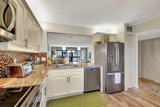 kitchen featuring appliances with stainless steel finishes, light wood-type flooring, backsplash, sink, and pendant lighting