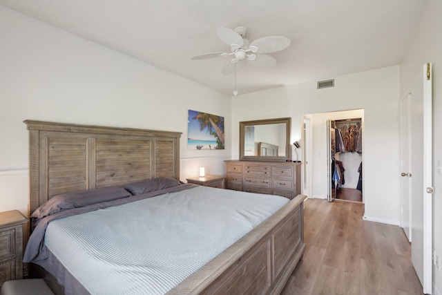 bedroom featuring ceiling fan, a walk in closet, light hardwood / wood-style flooring, and a closet