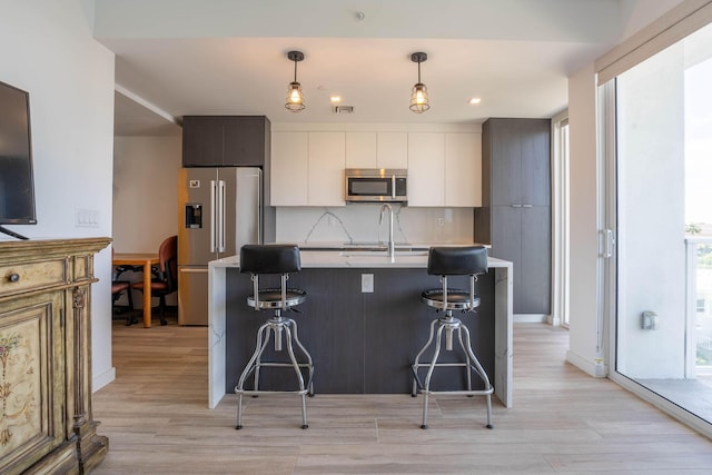 kitchen featuring tasteful backsplash, hanging light fixtures, appliances with stainless steel finishes, a kitchen island with sink, and white cabinets