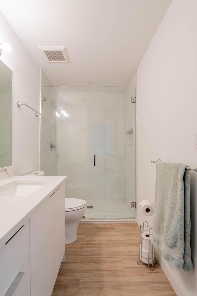 bathroom featuring vanity, hardwood / wood-style flooring, a shower with shower door, and toilet