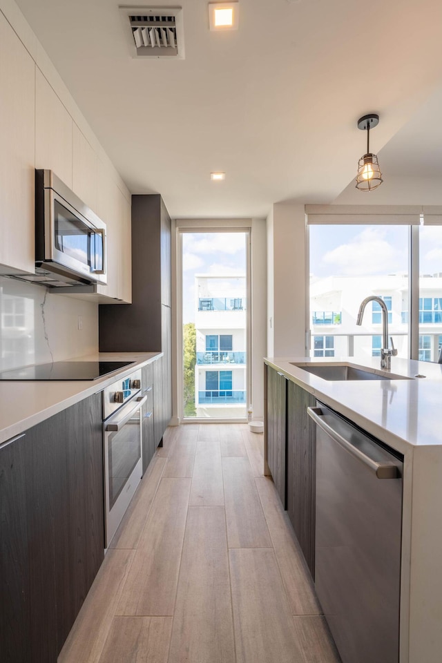 kitchen with pendant lighting, sink, light hardwood / wood-style flooring, appliances with stainless steel finishes, and white cabinets