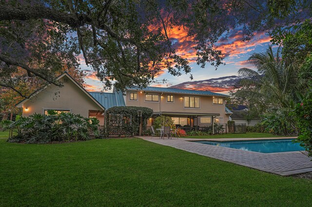 back house at dusk featuring a yard and a patio