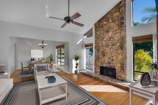 living room featuring hardwood / wood-style flooring, ceiling fan with notable chandelier, high vaulted ceiling, and a fireplace