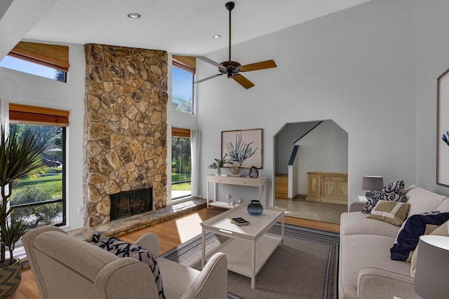 living room featuring hardwood / wood-style flooring, high vaulted ceiling, ceiling fan, and a stone fireplace