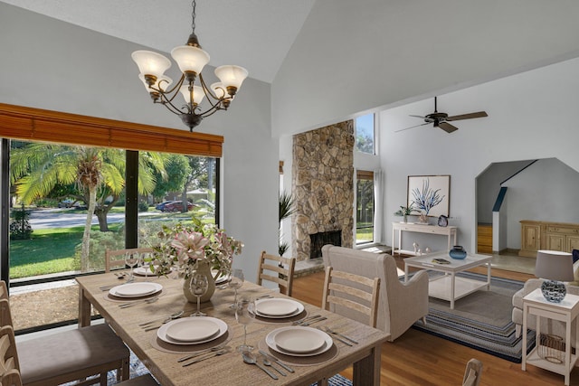 dining room with a fireplace, light wood-type flooring, ceiling fan with notable chandelier, and high vaulted ceiling