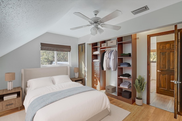 bedroom with light hardwood / wood-style floors, vaulted ceiling, a textured ceiling, a closet, and ceiling fan