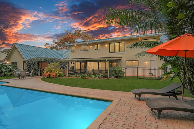 back house at dusk with a patio area, a fenced in pool, and a yard