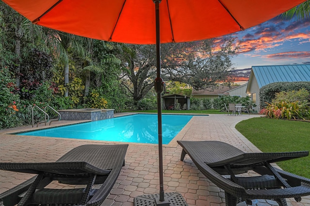 pool at dusk with a lawn, an in ground hot tub, and a patio