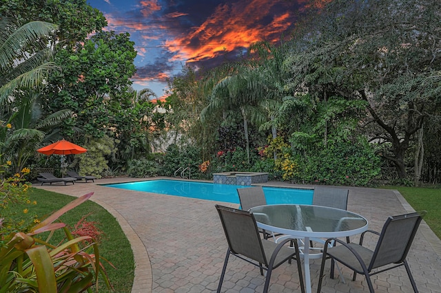 pool at dusk featuring an in ground hot tub and a patio