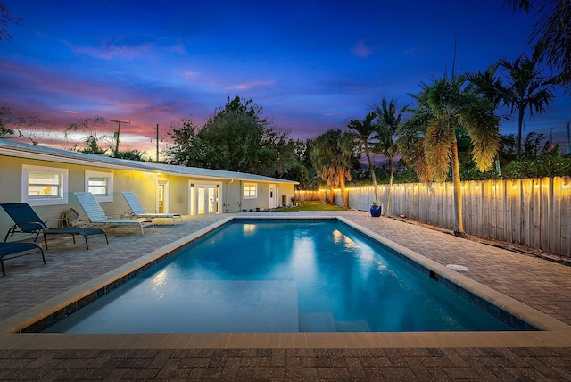 pool at dusk featuring french doors and a patio area