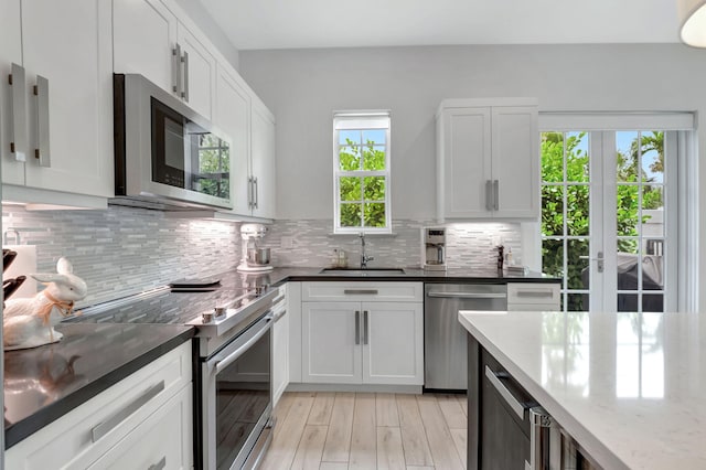 kitchen featuring white cabinets, sink, decorative backsplash, dark stone countertops, and stainless steel appliances