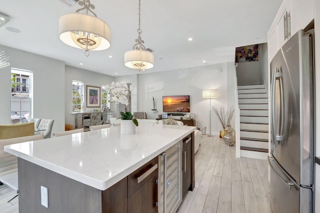 kitchen featuring dark brown cabinets, white cabinetry, light hardwood / wood-style floors, stainless steel refrigerator, and hanging light fixtures