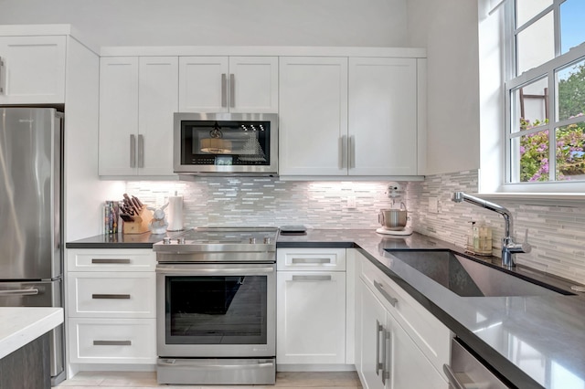 kitchen featuring appliances with stainless steel finishes, white cabinetry, a sink, and tasteful backsplash