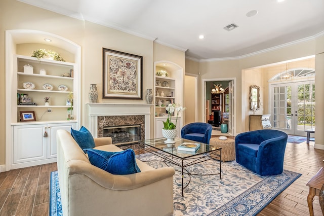 sitting room with an inviting chandelier, french doors, ornamental molding, built in features, and a fireplace