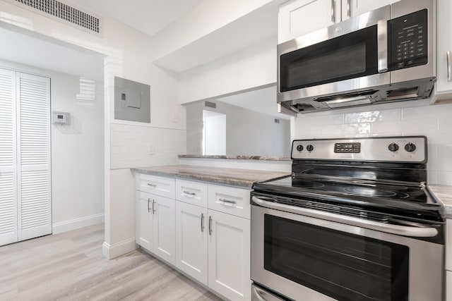 kitchen with stainless steel appliances, tasteful backsplash, light stone counters, electric panel, and white cabinets